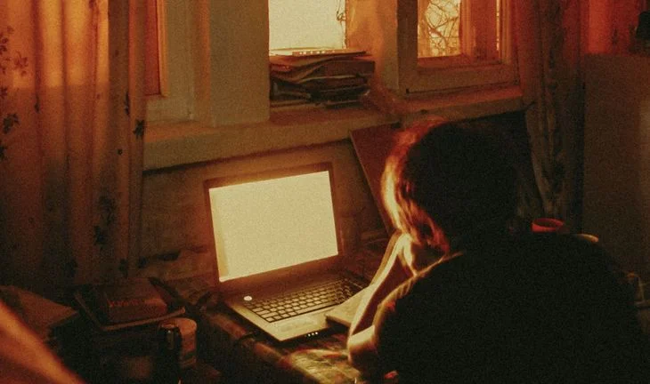 a boy looking at a laptop screen at dusk
