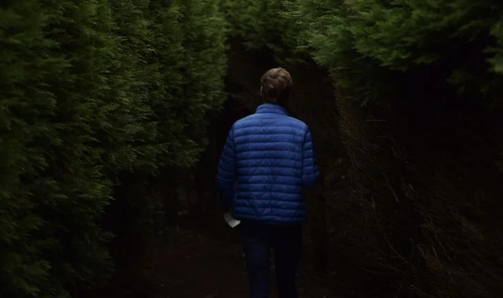 A man in a blue coat inside a hedge
